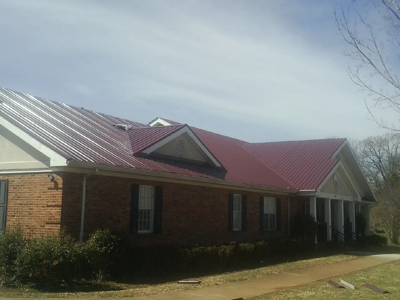 Red metal roof with gabled entries on a long brick building, from a Hail Damage Roof Repair job in Log Lane Village