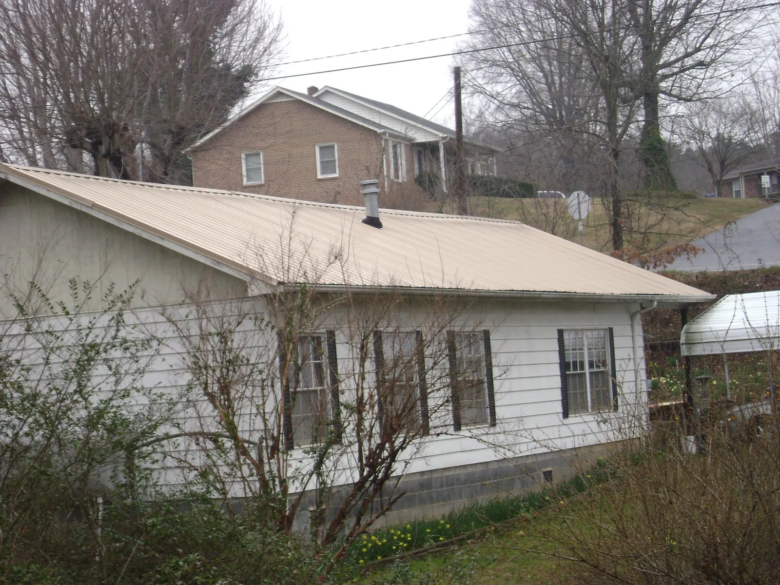 Tan metal roof on a white sided house set into a hillside — Commercial Roofing by Roofing Brothers in Log Lane Village