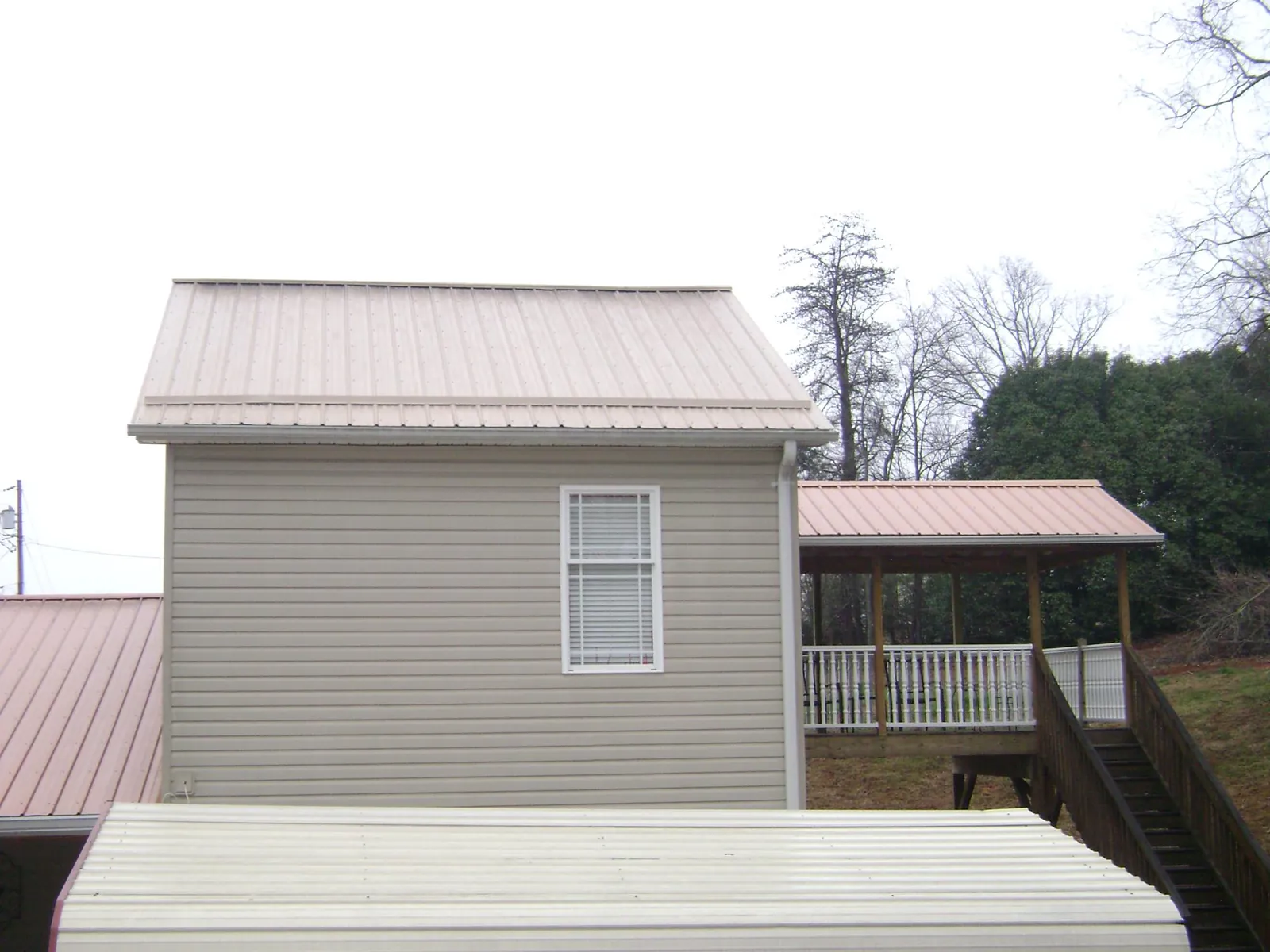 Tan metal roofs on a two story addition and attached porch, from a Roof Replacement job in Log Lane Village